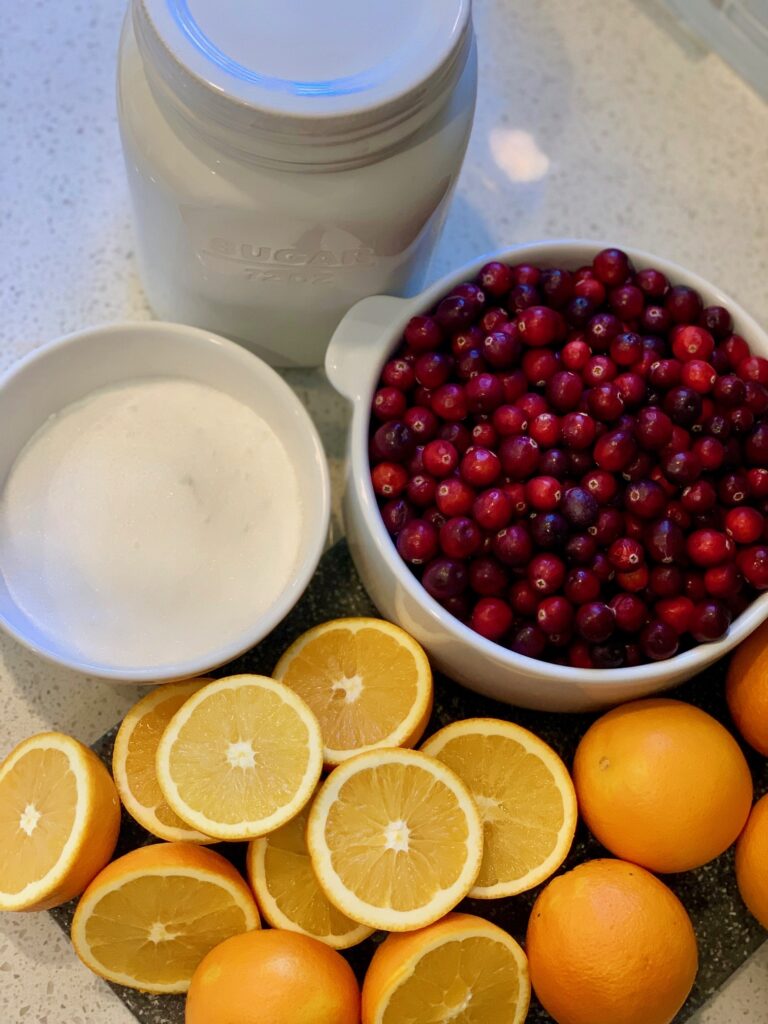 ingredients including bowl of cranberries, oranges, and sugar