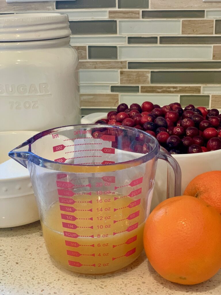 measuring cup of orange juice next to bowl of cranberries